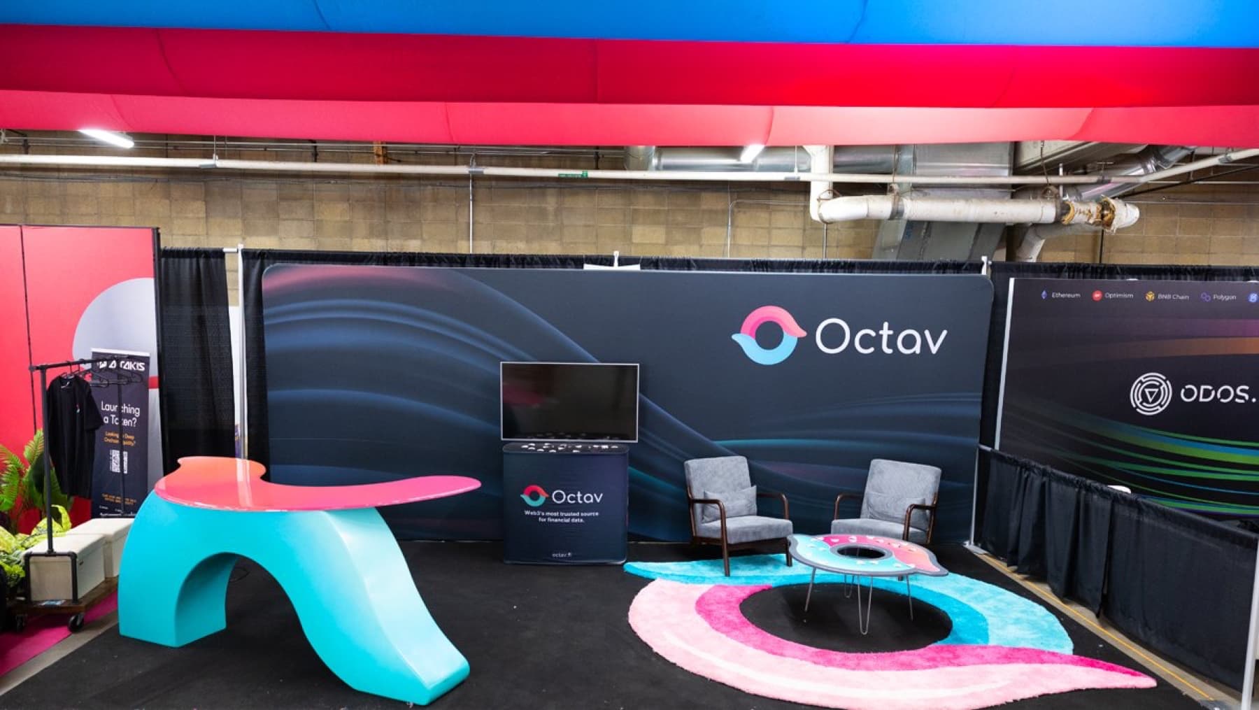 The Octav booth on the ETHDenver floor: wave counter, logo table, rug and backdrop